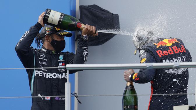 Pembalap Mercedes Lewis Hamilton (kiri) menyemprotkan sampanye kepada pembalap Red Bull Max Verstappen setelah memenangkan F1 GP Eifel di Nuerburgring, Nuerburg, Jerman, Minggu (11/10/2020). Hamilton dengan 91 kemenangannya menyamai legenda F1 Michael Schumacher. (Ronald Wittek, Pool via AP)