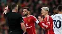 Gelandang Manchester United, Bruno Fernandes, bersama rekan setimnya, Alejandro Garnacho, melakukan protes terhadap wasit Chris Kavanagh, setelah pemain asal Portugal itu dikartu merah dalam laga kontra Tottenham Hotspur di Old Trafford, Minggu (29/9/2024). (Paul ELLIS / AFP)