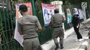 Petugas Satpol PP bersama Panwaslu kecamatan Ciracas menurunkan APK yang terpasang di pagar pembatas antara jalan dengan taman di pinggir kali di sekitar Jalan Raya Bogor, Jakarta, Rabu (23/1). (Liputan6.com/Helmi Fithriansyah)