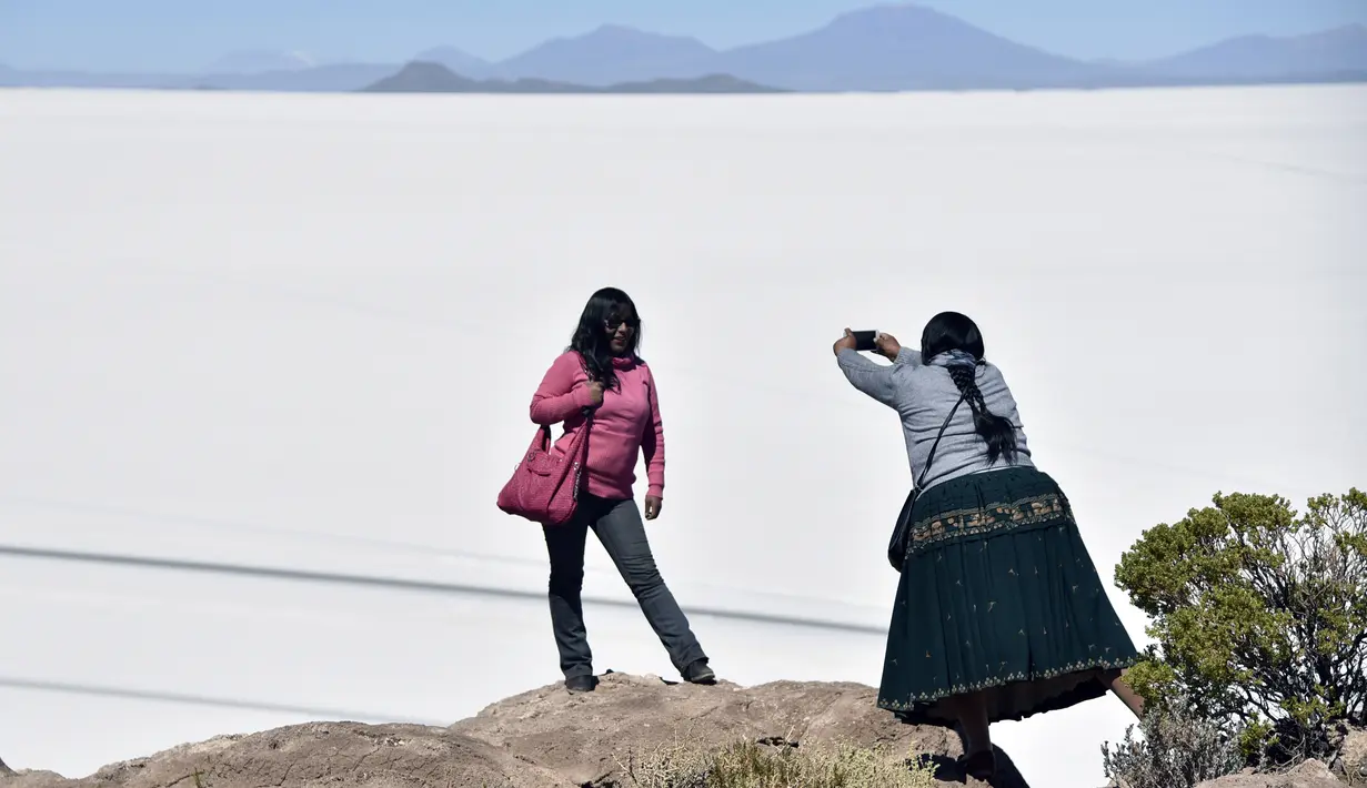 Turis berfoto dengan latar belakang Salar de Uyuni, dataran garam terluas di dunia yang terletak di Altiplano, barat daya Bolivia, 28 September 2019. Hamparan danau yang bisa dipijak itu begitu jernih sehingga membuat pantulan langit di atasnya. (Photo by Aizar RALDES / AFP)