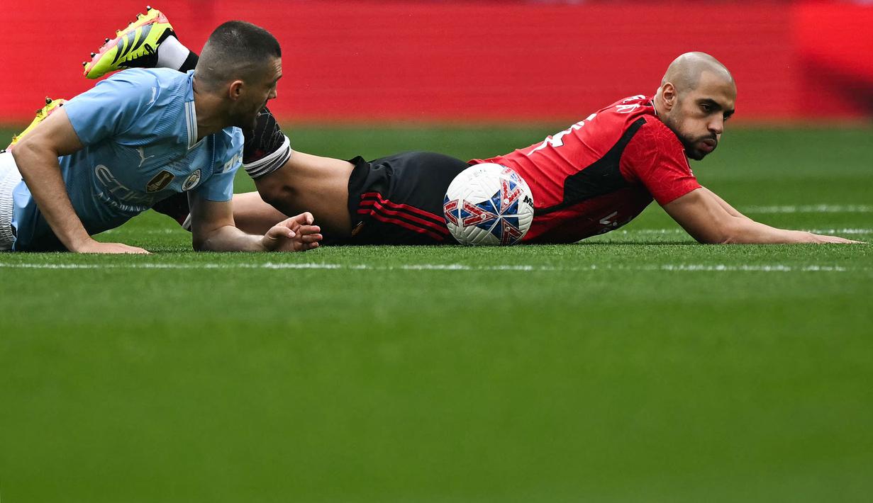 Pemain Manchester United, Sofyan Amrabat (kanan) terjatuh setelah berebut bola dengan pemain Manchester City, Mateo Kovacic saat laga final Piala FA 2023/2024 di Stadion Wembley, London, Sabtu (26/05/2024). (AFP/Ben Stansall)