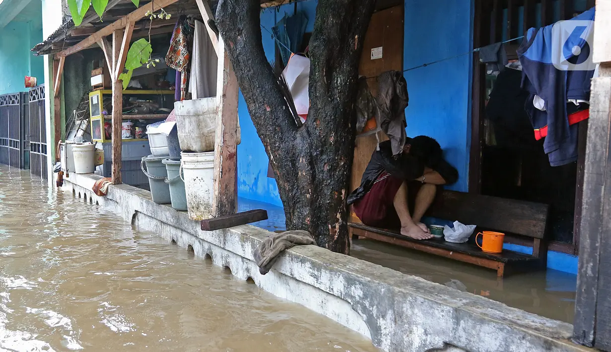 Warga duduk di atas bangku sebuah rumah saat banjir di RW 07, Kelurahan Pekayon, Jakarta Timur, Sabtu (20/2/2021). Banjir di kawasan tersebut terjadi akibat curah hujan yang tinggi. (Liputan6.com/Herman Zakharia)