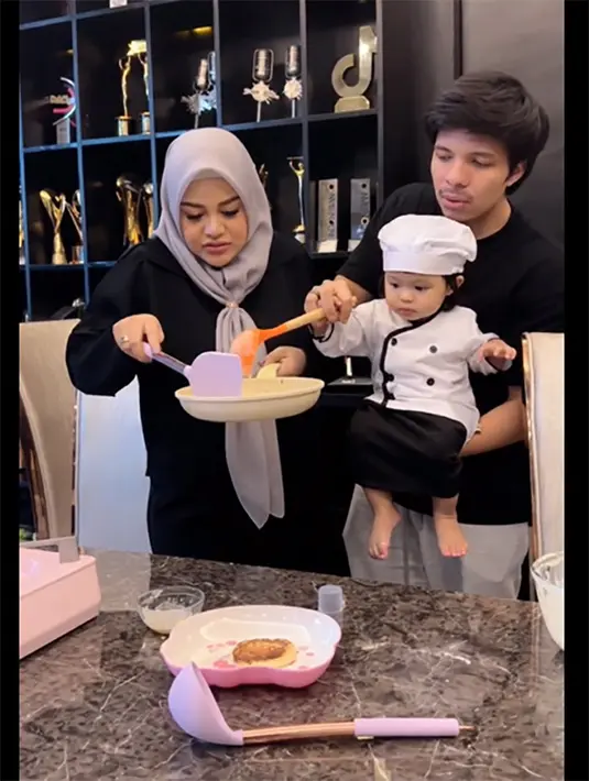 Mengikuti mamanya cara mengaduk adonan kue. Baby Ameena juga memiliki bakat seperti sang ayah, menyapa pemirsanya. "Hi guysss!! teriak Ameena dengan semangat. [Instagram/attahalilintar]