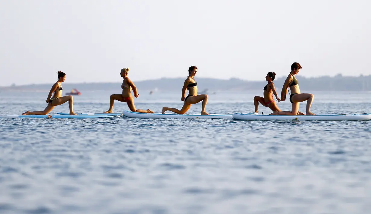 Sejumlah wanita mengenakan bikini saat melakukan gerakan yoga dengan papan seluncur di Laut Adriatic, Kroasia, Kamis (6/8/2015). (REUTERS/Pawel Kopczynski)