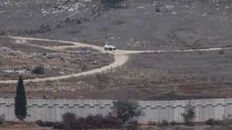 Israel berdalih bahwa tembok itu bagian dari rencana militer yang lebih luas, yang pembangunannya dimulai pada 2022 lalu. Tampak dalam foto yang diambil dari Israel, menunjukkan kendaraan Pasukan Sementara PBB di Lebanon (UNIFIL) yang sedang berpatroli di sisi Lebanon dari perbatasan yang memisahkan Israel utara dan Lebanon selatan pada 16 November 2025. (Jalaa MAREY/AFP)