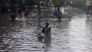 Seorang pria berbicara di ponselnya sambil mendorong motornya di sepanjang jalan yang banjir setelah hujan lebat di Lahore (16/7/2019).Banjir bandang merusak lebih dari 120 rumah, 30 toko dan melumpuhkan pasokan air dan listrik. (AFP Photo/Arif Ali)