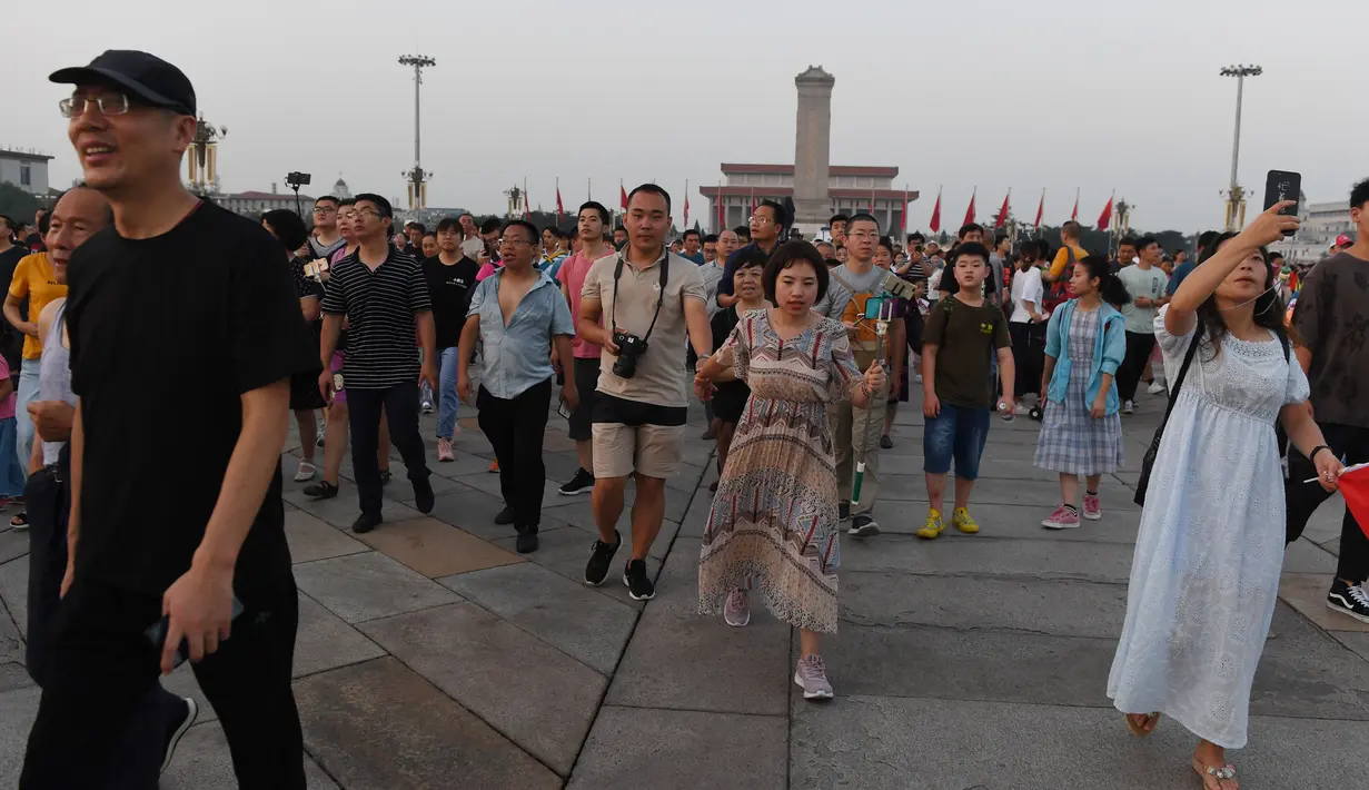 Warga berjalan menghadiri upacara pengibaran bendera saat fajar setelah kematian mantan perdana menteri China Li Peng di Lapangan Tiananmen Beijing (24/7/2019). Li Peng biasa dikenal sebagai "Jagal Beijing" meninggal di usia 90 tahun. (AFP Photo/Greg Baker)