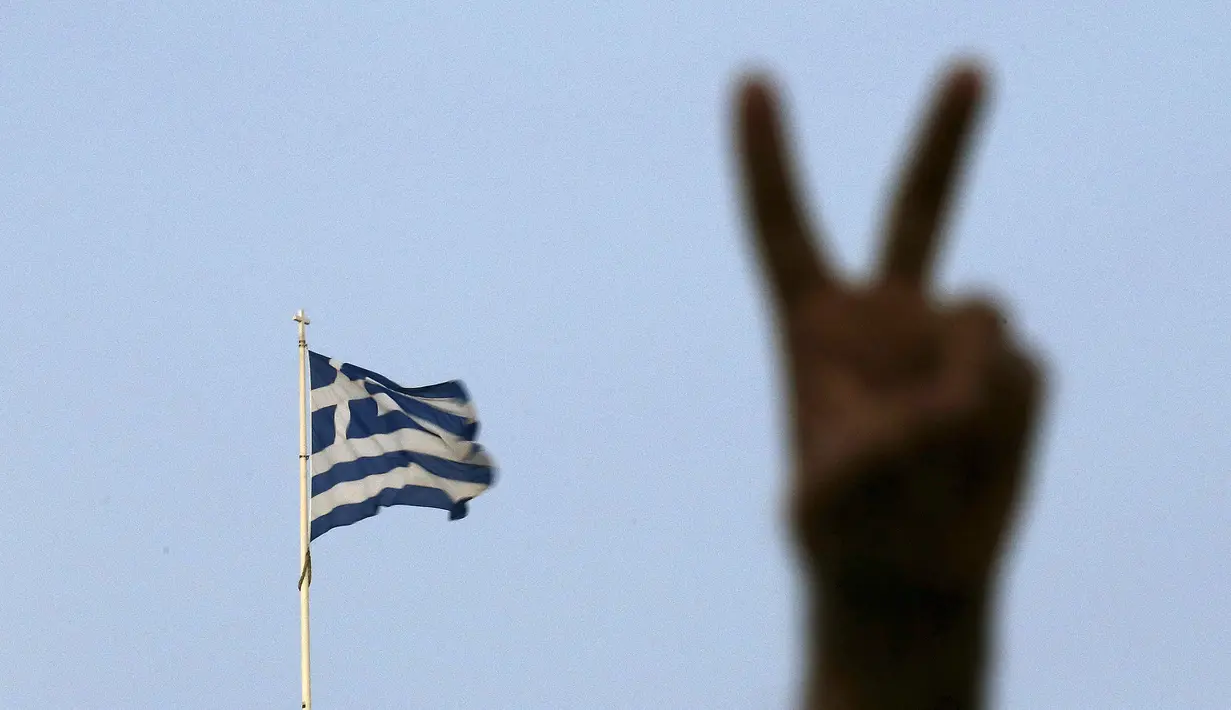 Seorang pendukung mengangkat tangan tanda kemenangan disamping bendera Yunani atas parlemen di Athena, Yunani (6/7/2015).  Parlemen Eropa Heald sidang paripurna pada tanggal 7 Juli pada konsekuensi dari hasil referendum Yunani.  (REUTERS/Yannis Behrakis)