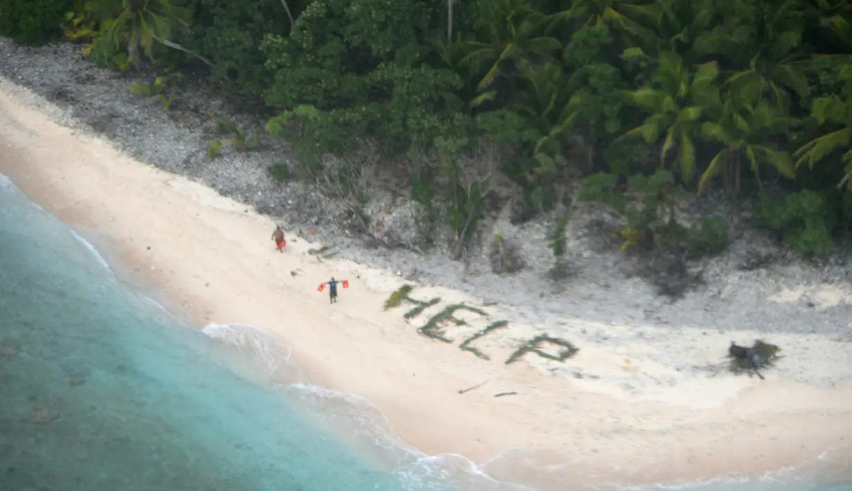 Dua orang berdiri disamping tulisan "Help" yang tersusun dari dahan pohon palem di pulau tak berpenghuni Faradik, Mikronesia, 7 April 2016. Tiga orang pelaut berhasil diselamatkan pasukan AL Amerika Serikat setelah tiga hari terdampar. (AFP Photo)