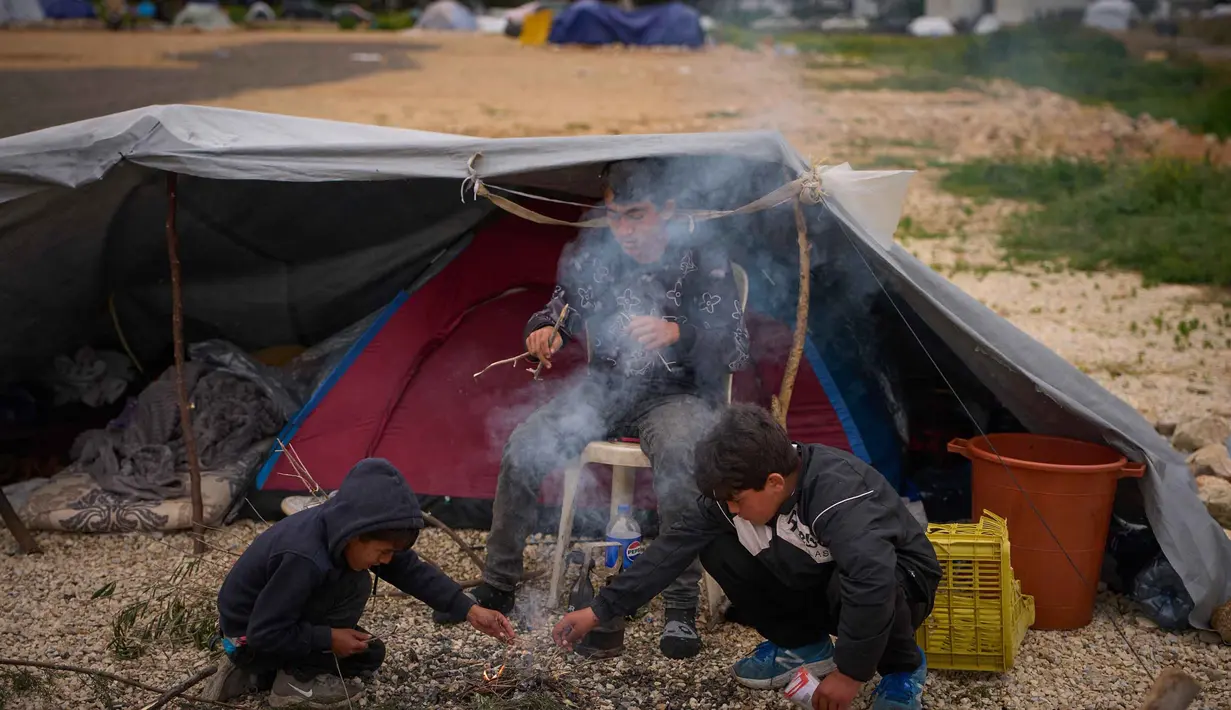 Anak-anak pengungsi yang melarikan diri bersama keluarga mereka dari serangan artileri Israel di Lebanon selatan membuat api unggun di samping tenda yang digunakan sebagai tempat berlindung di Beirut, Lebanon, Rabu, 1 April 2026. Di tengah meningkatnya serangan udara Israel, gelombang pengungsi di Lebanon terus bertambah. (AP Photo/Emilio Morenatti)