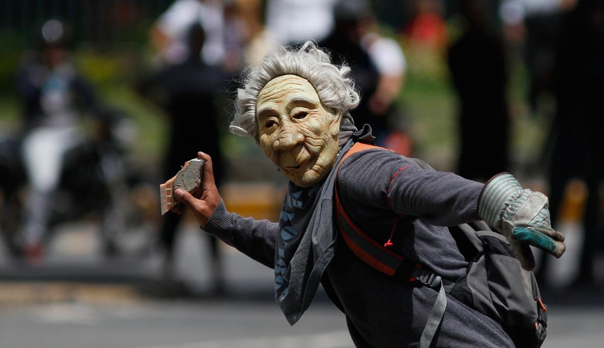 Seorang pengunjuk rasa memakai topeng, bersiap melempar batu saat mereka bentrok dengan polisi antihuru-hara menuntut Presiden Venezuela, Nicolas Maduro di Caracas (10/7). (AP Photo/Ariana Cubillos)