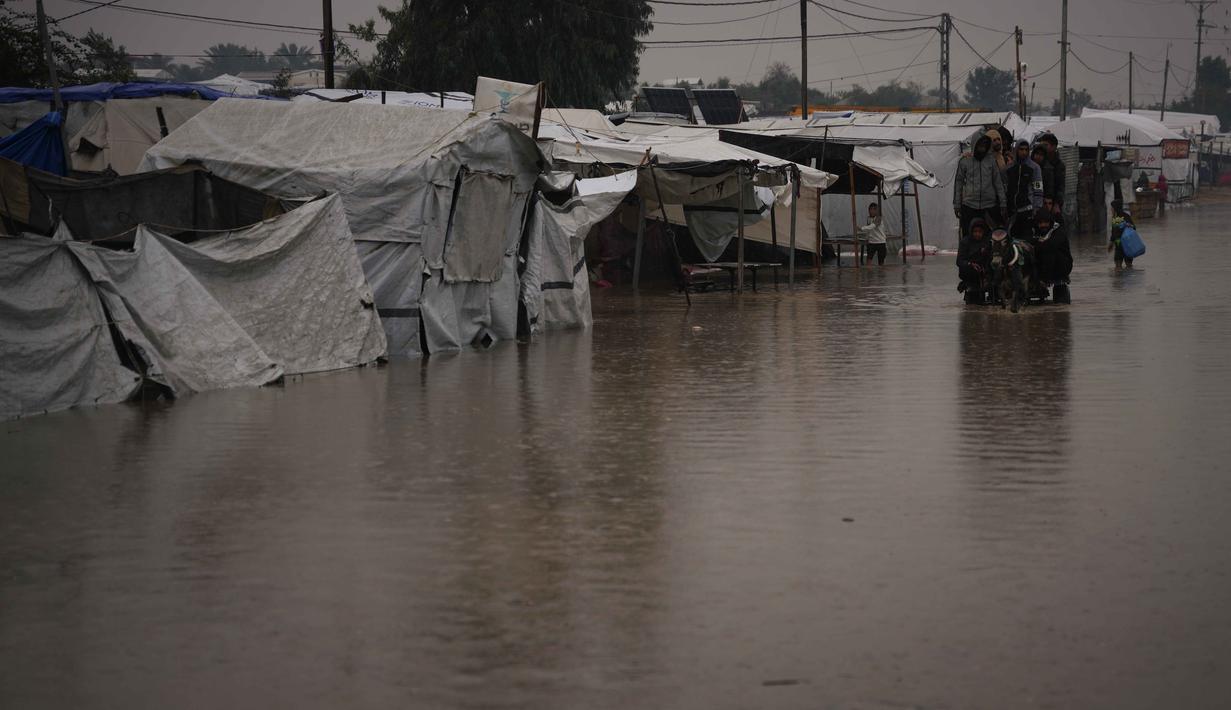 Warga Palestina menyeberangi jalan yang tergenang banjir setelah hujan lebat di Khan Younis, Jalur Gaza selatan, Kamis 11 Desember 2025. Hujan deras di Khan Younis menyebabkan kondisi kemanusiaan di kamp-kamp pengungsi menjadi sangat kritis. (AP Photo/Abdel Kareem Hana)