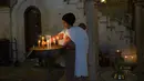 Seorang wanita menyalakan lilin dengan bayinya di punggung saat misa Kamis Putih di Kota Tua Yerusalem, Kamis (1/4/2021). Kamis Putih adalah hari Kamis sebelum Paskah dimana umat Kristen memiliki tradisi memperingati Perjamuan Malam terakhir yang dipimpin Yesus. (AP Photo/Maya Alleruzzo)
