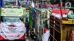 Salah satu peserta aksi terlihat di antara truk-truk saat unjuk rasa terkait Rancangan Undang Undang (RUU) nol kelebihan muatan dan dimensi atau Zero Over Dimension Over Load (ODOL) memasang spanduk di Jalan Medan Merdeka Selatan, Jakarta, Rabu (2/7/2025). (Liputan6.com/Herman Zakharia)