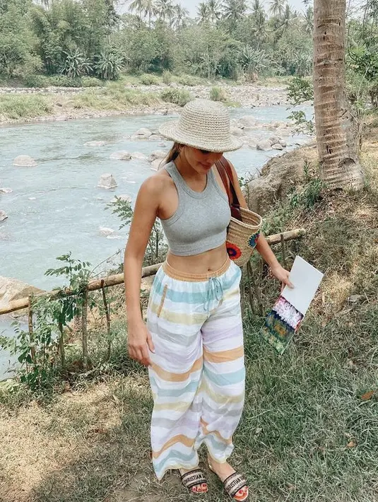 Luna maya mengenakan tank top helter neck crop top abu-abu dikombinasikan loose pants bergaris warna-warni.  (@lunamaya)