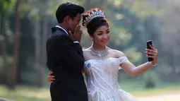 Sepasang pengantin baru berswafoto saat disela pengambilan foto pernikahan mereka di kompleks kuil Angkor Wat, sebuah candi ikonik dan bersejarah di Kamboja, 14 Maret 2018. Candi ini masuk dalam daftar Situs Warisan Dunia UNESCO. (AP Photo/Heng Sinith)