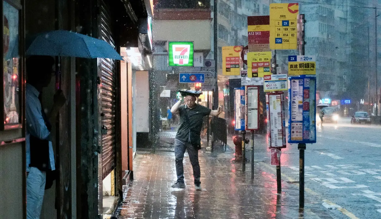 Seorang pejalan kaki menutupi kepalanya dengan tas di samping salah satu halte bus kawasan Quarry Bay, Hong Kong, pada 5 Agustus 2025, di tengah peringatan hujan badai hitam yang dikeluarkan oleh observatorium cuaca kota. (Tommy WANG/AFP)