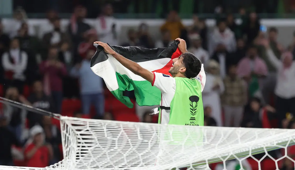 Pemain Yordania, Yazan Al-Naimat membentangkan bendera negaranya saat merayakan kemenangan timnya atas Korea Selatan setelah laga semifnial Piala Asia 2023 di Ahmad Bin Ali Stadium, Doha, Qatar, Selasa (06/02/2024). (AFP/Giuseppe Cacace)