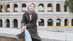 Berlibur ke Colosseum di Roma, Italia, Gita mengenakan coat berwarna abu-abu yang dipadukan dengan hijab segiempat berwarna taro, celana jeans, dan sneakers. (Liputan6.com/IG/@gitasav)