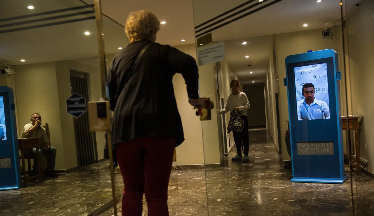 Seorang wanita memasuki sebuah gedung di Buenos Aires, Argentina, Senin (23/4). Penjaga keamanan virtual memantau setiap pengunjung yang ingin keluar masuk gedung. (AP Photo/Rodrigo Abd)