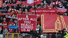 Penggemar Liverpool memegang poster yang mengejek skandal keuangan Manchester City saat kru televisi bekerja di tepi lapangan menjelang pertandingan Liga Inggris antara Liverpool dan Manchester City di Anfield di Liverpool, barat laut Inggris pada 11 Oktober 2026. Manchester City menghadapi Anfield yang bermusuhan pada hari Minggu ketika pemimpin Premier League itu menghadapi rival sengitnya Liverpool dalam pertandingan pertama mereka sejak dinyatakan bersalah karena melanggar lebih dari 100 aturan keuangan. (Paul ELLIS/AFP)