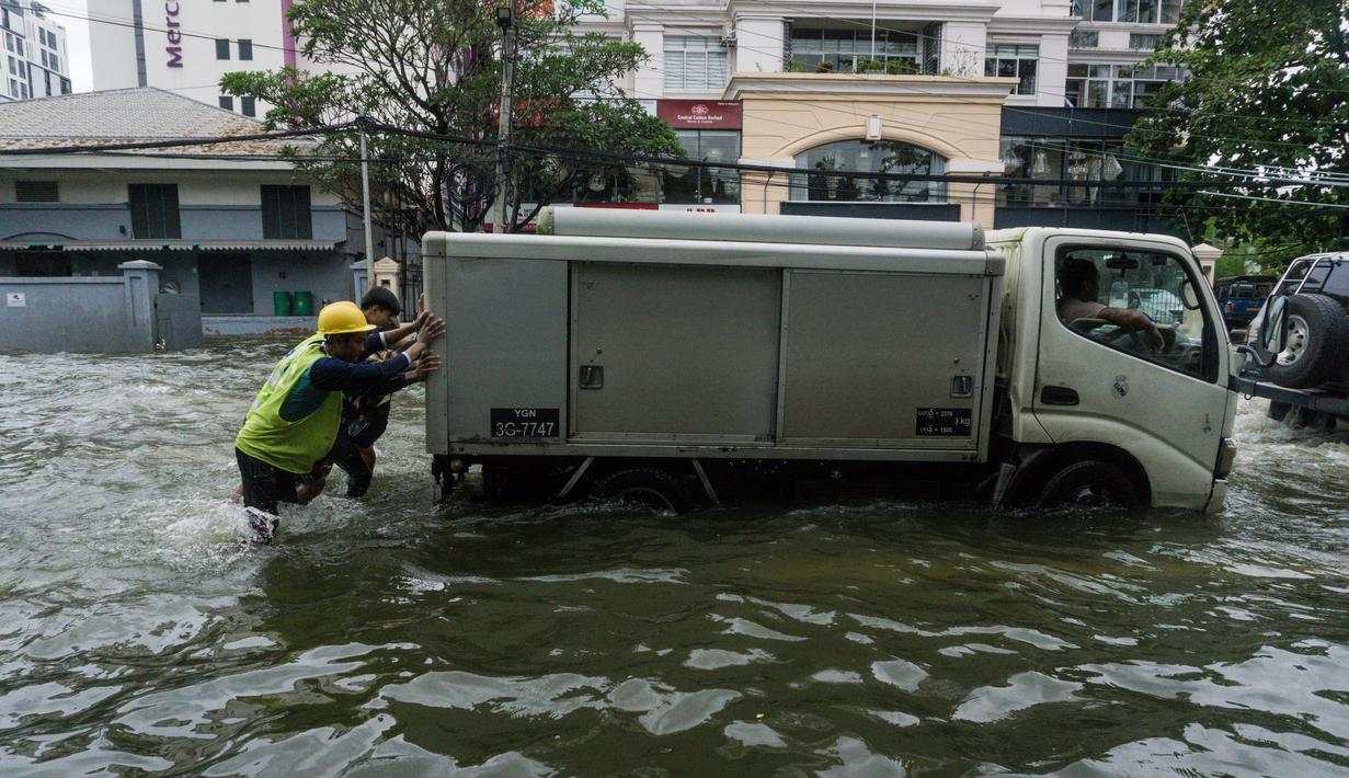 Orang-orang mendorong kendaraan yang mogok di jalan yang banjir di pinggiran Yangon, Myanmar  (17/8/2022). Hujan lebat sejak larut malam 16 Agustus menyebabkan kemacetan lalu lintas dan kesulitan bagi para komuter di kota Yangon dengan beberapa jalan masih terendam banjir.  (AFP/Stringer)