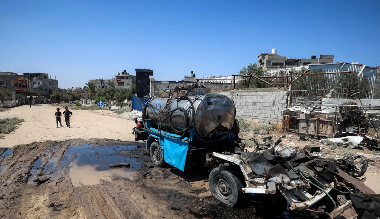 Seorang anak laki-laki mengambil air ke dalam jeriken dari kendaraan mobile tangki air yang hancur akibat pengeboman Israel di kamp Nuseirat untuk pengungsi Palestina di Jalur Gaza tengah pada 14 Juli 2025. (Eyad BABA/AFP)