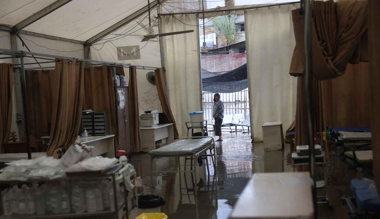 Saat ini, pengungsi Palestina di Gaza menghadapi kondisi yang semakin sulit, terdampak cuaca ekstrem dan kekurangan tempat berlindung yang layak. Tampak dalam foto, kondisi ini memperparah krisis kemanusiaan di wilayah tersebut. Tampak dalam foto, seorang pengungsi Palestina melihat genangan air di dalam tenda darurat milik Rumah Sakit Nasser, yang berfungsi sebagai tempat penerimaan pasien rawat jalan dan departemen gawat darurat, setelah hujan deras di Khan Yunis di Jalur Gaza selatan pada 26 Maret 2026. (Bashar Taleb/AFP)