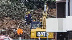 Polisi dan petugas yang berdiri setelah tanah longsor sementara pencarian sedang dilakukan oleh layanan darurat setempat untuk orang hilang di Gunung Maunganui, Tauranga, Selandia Baru pada Kamis 22 Januari 2026. Hujan lebat yang mengguyur Selandia Baru menyebabkan sejumlah kerusakan dan memicu longsor. (DJ MILLS/AFP)