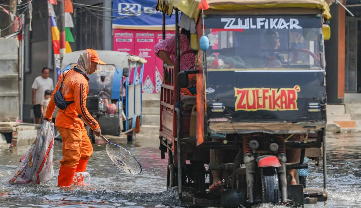 Petugas Penanganan Prasarana dan Sarana Umum (PPSU) membersihkan sampah pada genangan air rob yang melanda wilayah Muara Angke, Jakarta Utara, Selasa (19/11/2024). (merdeka.com/Arie Basuki)