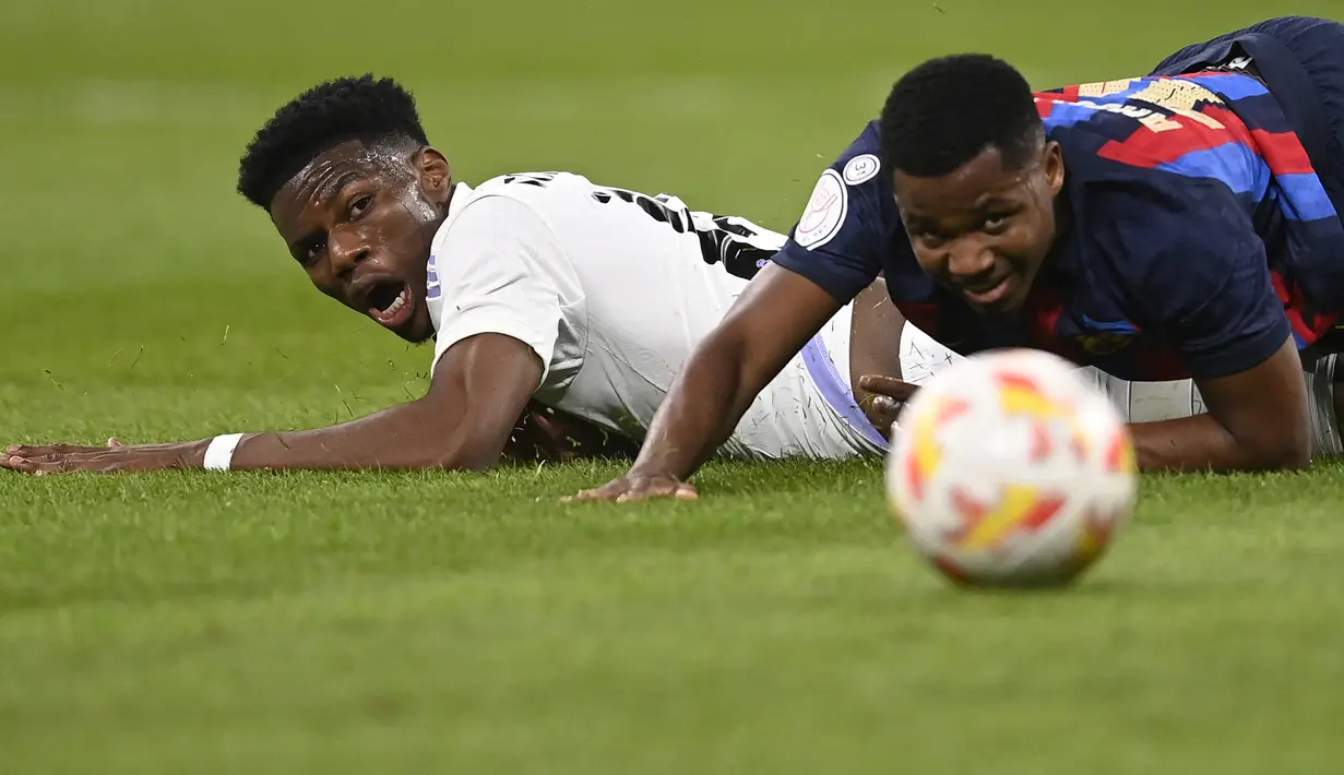 Bek Real Madrid, Aurelien Tchouameni (kiri) dan striker Barcelona, Ansu Fati terjatuh dalam perebutan bola pada laga leg pertama semifinal Copa del Rey 2022/2023 di Santiago Bernabeu Stadium, Madrid (2/3/2023). Aurelien Tchouameni baru memasuki musim pertama bersama Real Madrid sejak didatangkan pada awal musim 2022/2023. Musim ini ia telah tampil dalam 40 laga di semua ajang bareng Los Blancos dengan torehan 4 assist. (AFP/Oscar Del Pozo)