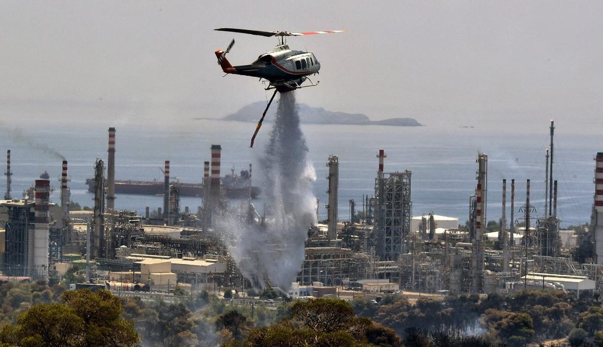 <p>Helikopter pemadam kebakaran menyemprotkan air saat terjadi kebakaran hutan dekat kilang minyak di Agioi Theodoroi. (Valerie GACHE/AFP)</p>