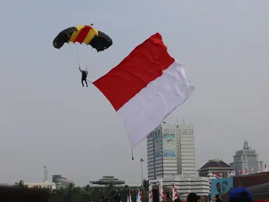Personel Polri membawa bendera merah putih saat atraksi terjun payung pada peringatan HUT Bhayangkara ke-71 di Silang Monas, Jakarta, Senin (10/7). Acara ini menampilkan berbagai atraksi dari masing-masing kesatuan Polri. (Liputan6.com/Angga Yuniar)