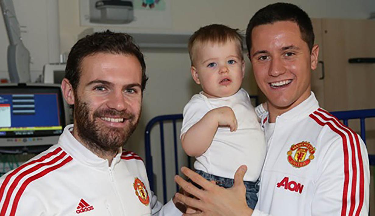 Pemain Manchester United, Ander Herrera, menggendong seorang anak yang sedang sakit saat mengunjungi Rumah Sakit Royal Manchester Children bersama rekan setimnya, Juan Mata. (www.manutd.com)