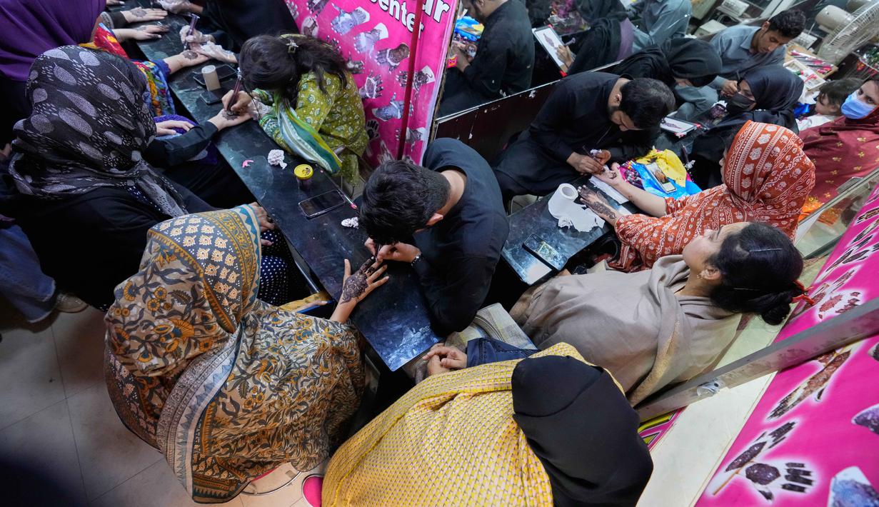 Wanita dan anak-anak akan mengunjungi pasar yang buka hingga larut malam untuk mengantre di stan seniman henna. Tampak dalam foto, para ahli kecantikan, di bagian atas, melukis 'Henna' tradisional di tangan pelanggan untuk perayaan Idul Fitri, yang menandai berakhirnya bulan suci Ramadan, di Rawalpindi, Pakistan, Rabu, 18 Maret 2026. (AP Photo/Anjum Naveed)