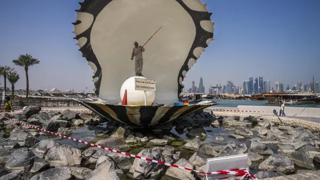 A migrant laborer paints The Pearl Monument, a sculpture depicting an open oyster shell with running water, on the corniche, overlooking the skyline of Doha, Qatar, Wednesday, Oct. 19, 2022.