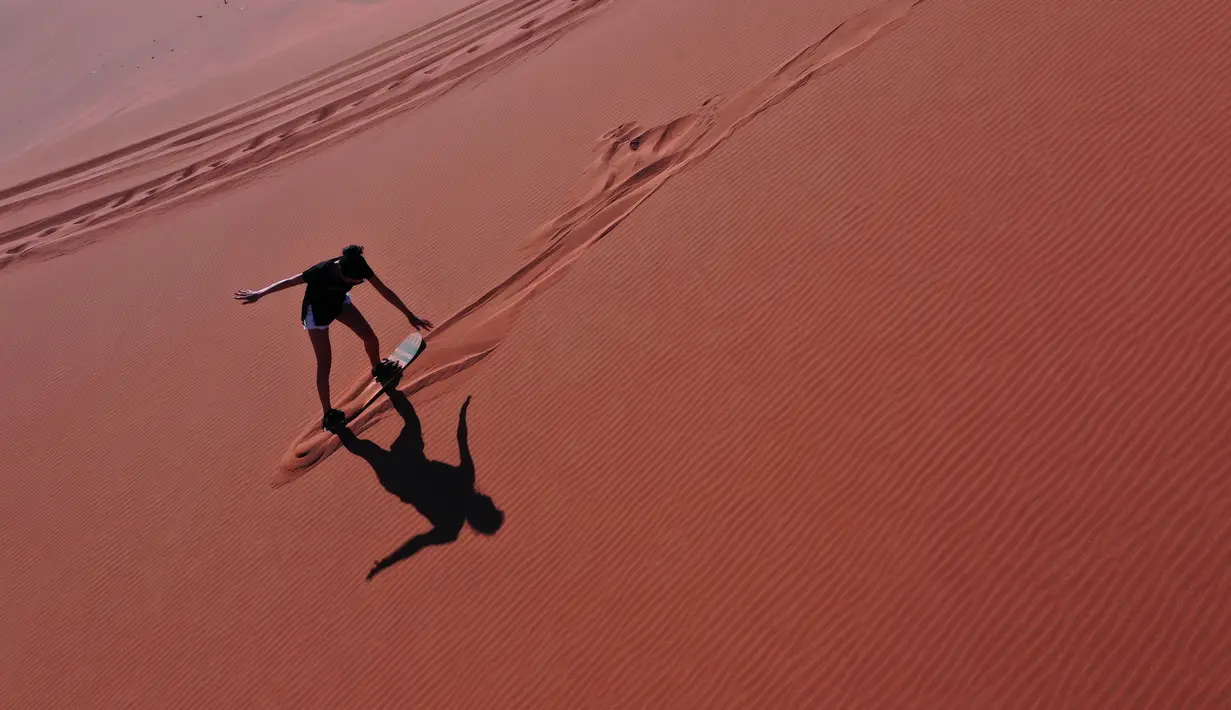 Aksi turis bermain sandboarding (papan seluncur) di gurun Dubai pada 11 Januari 2021. Di sini para wisatawan dapat mencoba sensasi bermain sandboarding sambil memandang hamparan lautan pasir cokelat. (Photo by GIUSEPPE CACACE / AFP)