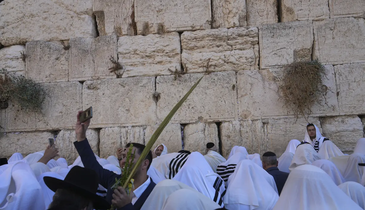 Seorang pria mendokumentasikan dengan ponselnya sebagai pria Yahudi ultra-Ortodoks dari kasta Cohanim Priestly berdoa tertutup selendang saat mereka berpartisipasi dalam pemberkatan selama hari raya Yahudi Sukkot di Tembok Barat, situs paling suci di mana orang Yahudi dapat berdoa, di Kota Tua Yerusalem Rabu, 12 Oktober 2022. (AP Photo/Tsafrir Abayov)