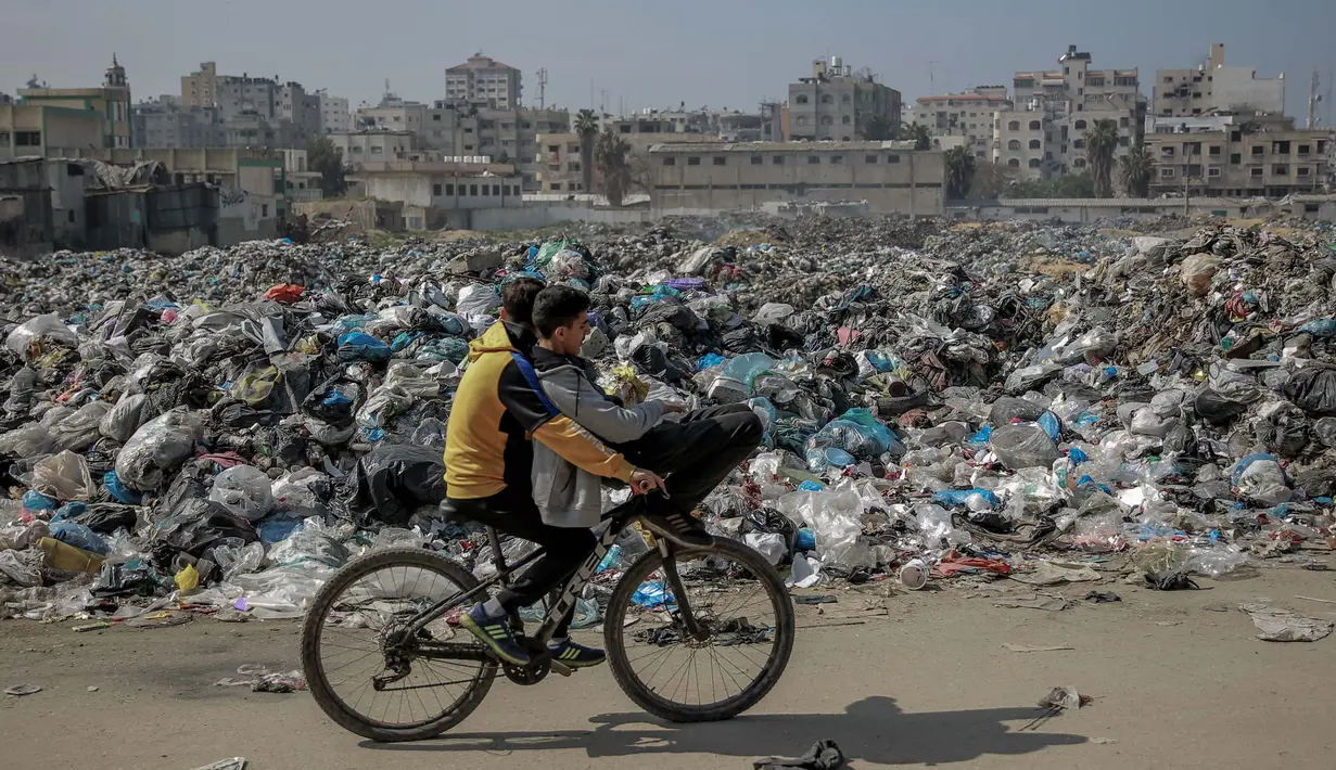 Anak-anak Palestina mengayuh sepeda melewati tempat pembuangan sampah besar di sepanjang jalan utama di Kota Gaza pada 24 Februari 2024. (Foto oleh AFP)