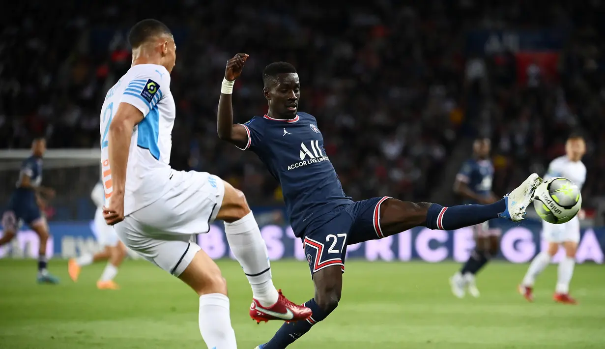 Gelandang Paris Saint-Germain (PSG) Idrissa Gueye (kanan) berebut bola dengan bek Olympique Marseille William Saliba pada laga Liga Prancis pekan ke-32 di Parc des Princes, Senin (18/4/2022) dini hari WIB. PSG vs Marseille berakhir dengan skor 2-1. (FRANCK FIFE / AFP)