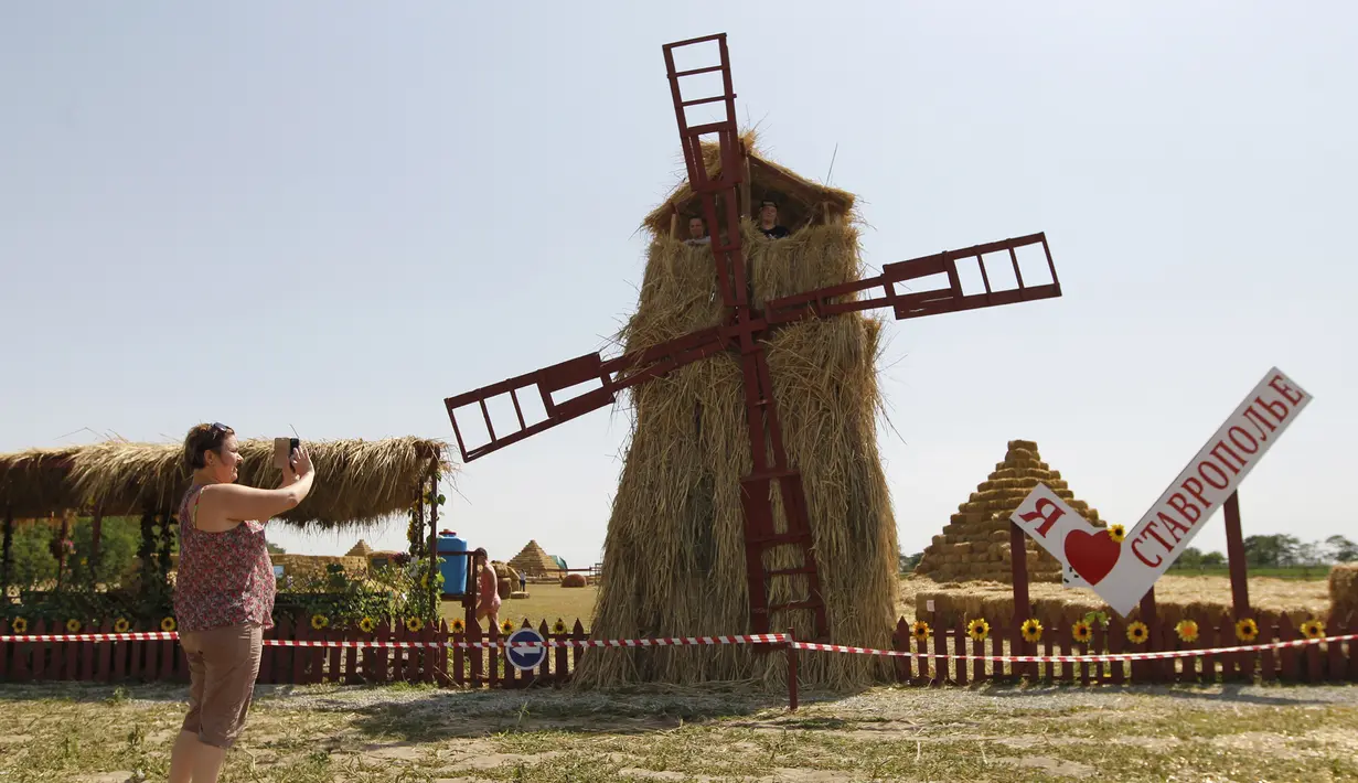 Pengunjung mengambil gambar kincir angin yang terbuat dari jerami di permukiman Krasnoye, Stavropol, Rusia, Rabu (19/7). Seluruh arena bermain pada taman tersebut terbuat dari tumpukan jerami. (REUTERS/Eduard Korniyenkov)