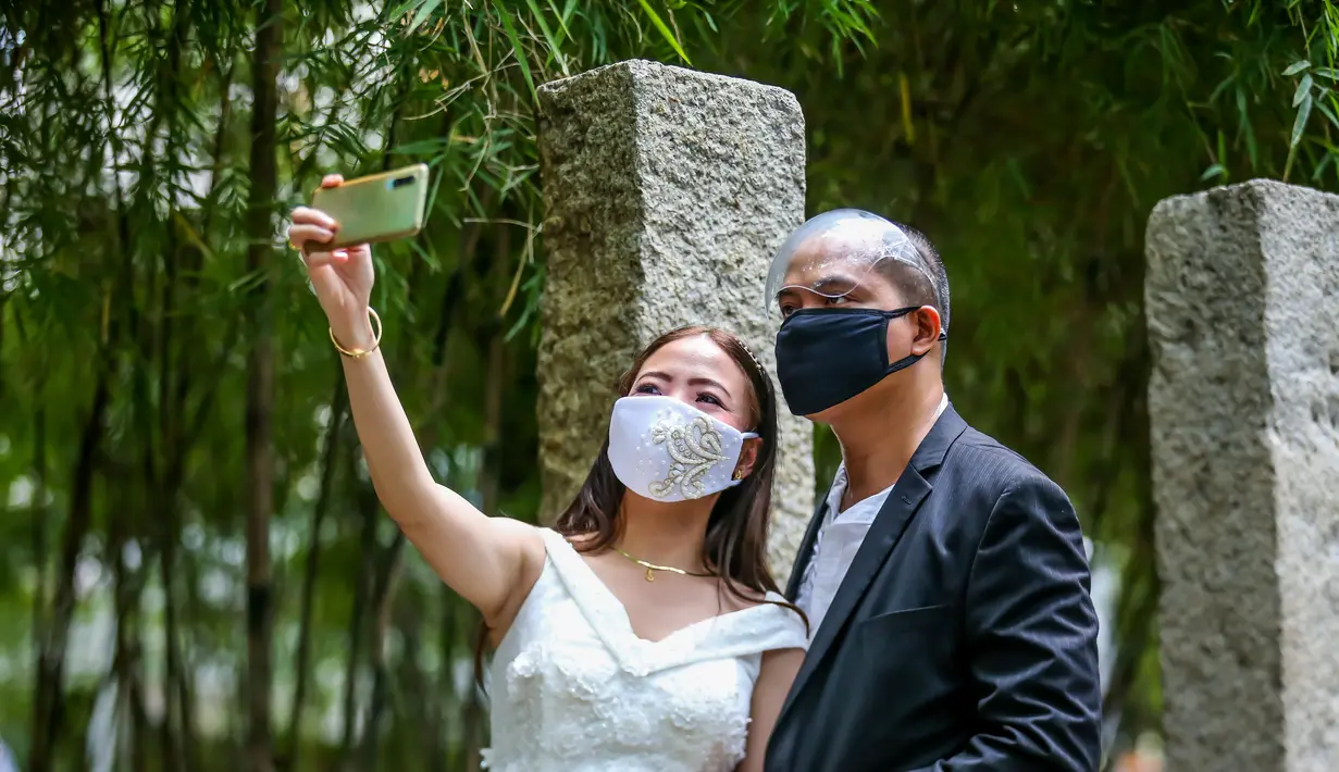 Pasangan berselfie dalam "pernikahan massal bermasker" di sebuah taman di Kota Makati, Filipina (15/12/2020). Pemerintah Filipina telah memberlakukan kebijakan untuk penggunaan masker di tengah kekhawatiran lonjakan kasus COVID-19 selama musim liburan. (Xinhua/Rouelle Umali)