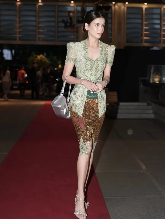 Sabrina Chairunnisa mengenakan kebaya brokat warna hijau lengan pendek dipadukan obi hijau. Kebaya buatan Intan Avantie ini dipadukan bawahan kain batik pendek. Ia membawa tas silvernya. [@sabrinachairunnisa_]