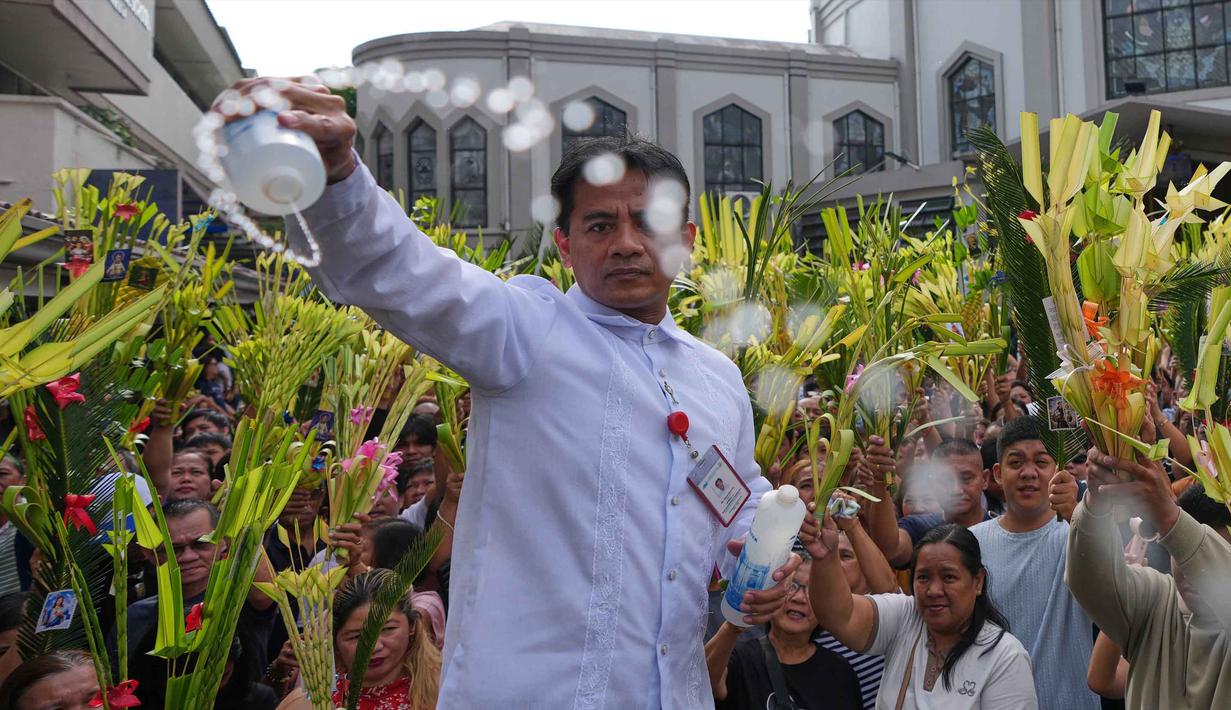 Hari ini, Minggu 29 Maret 2026, juga menandai awal Pekan Suci, peralihan dari masa Prapaskah menuju kisah sengsara, wafat, dan kebangkitan Yesus Kristus. Tampak dalam foto, seorang pekerja gereja memercikkan air suci ke daun palem para umat selama upacara pemberkatan di luar Katedral Antipolo, kota Antipolo, provinsi Rizal, Filipina, saat memperingati Minggu Palma, 29 Maret 2026. (AP Photo/Aaron Favila)