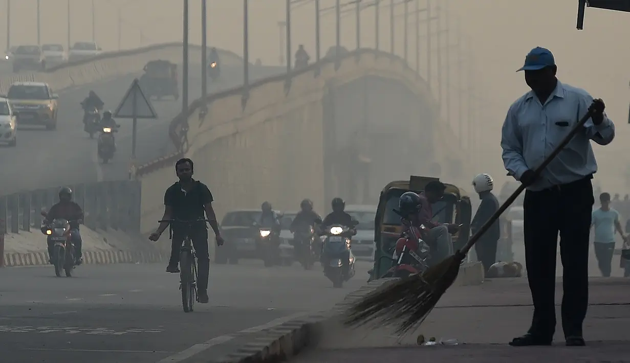 Petugas membersihkan jalan di tengah kondisi kabut asap tebal di New Delhi (30/10). Tingkat kabut melonjak selama musim dingin di Delhi, ketika kualitas udara sering melampaui tingkat aman Organisasi Kesehatan Dunia. (AFP Photo/Prakash Singh)