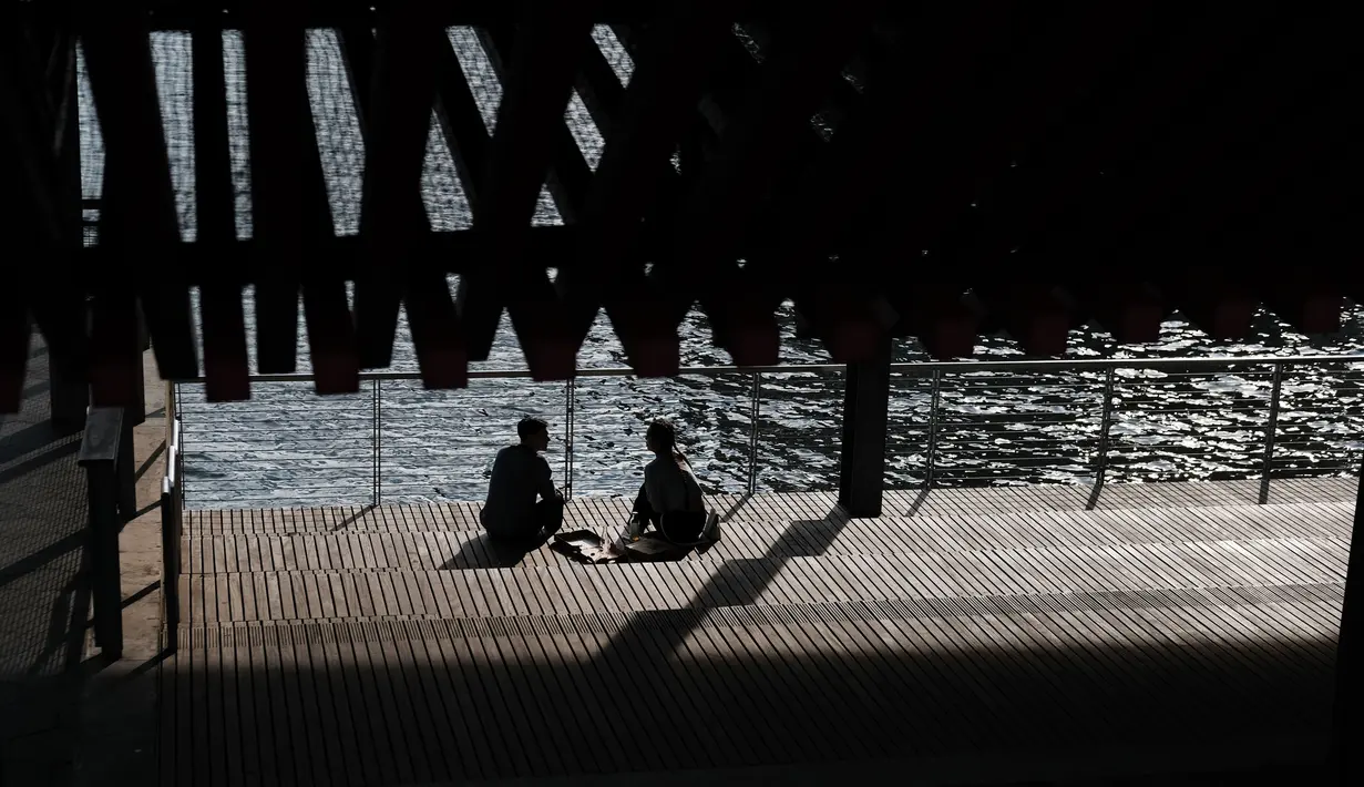 Pasangan berbincang saat menikmati musim semi yang hangat di tepi air di Manhattan di New York City (8/4). Sebagian besar Pantai Timur mengharapkan suhu hangat terus sepanjang minggu. (Spencer Platt/Getty Images/AFP)