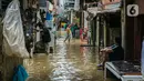 Seorang pria duduk di depan rumah saat warga lainnya membersihkan barang-barang yang terendam banjir di permukiman kawasan Kampung Melayu, Jakarta, Selasa (9/2/2021). Banjir yang berangsur surut dimanfaatkan warga untuk membersihkan rumah dan barang-barang. (Liputan6.com/Faizal Fanani)