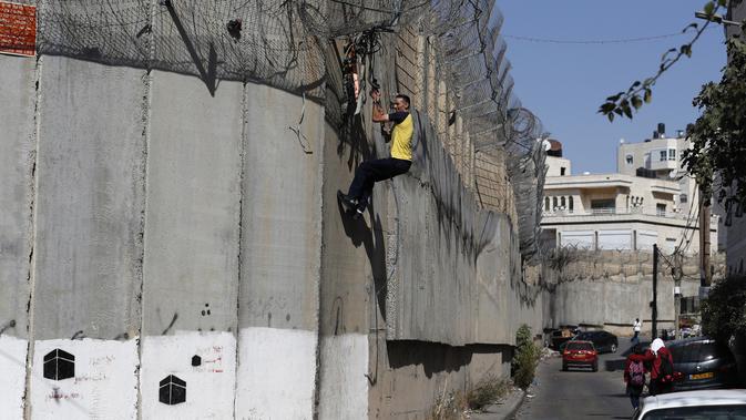 Seorang pria Palestina memanjat pagar perbatasan yang memisahkan Tepi Barat dengan Yerusalem di Distrik Beit Hanina, Yerusalem, Senin (7/10/2019). Banyak warga Palestina dari Tepi Barat menyeberang secara ilegal ke Israel setiap hari untuk mencari pekerjaan. (AHMAD GHARABLI/AFP)