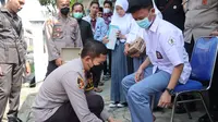 Kapolres Garut AKBP Wirdhanto Hadicaksono terpaksa bertekuk lutut membetulkan tali sepatu milik pelajar disela-sela pemberian sepatu korban banjir bandang Garut di kantor desa Jayaraga. (Liputan6.com/ Jayadi Supriadin)
