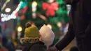 Seorang anak menyantap permen kapas di pasar Natal di St. Petersburg (20/12/2020). Wisatawan juga dapat mengunjungi konser dadakan, roti jahe, mainan, gua, dan wahana pasar malam. (Xinhua/Irina Motina)